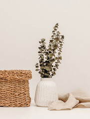 Vase with eucalyptus leaves, linen cloth and wicker container, cozy home decoration. Hygge style...