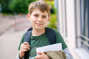 Happy preteen kid boy with backpack or satchel. Schoolkid in on the way to elementary or middle school on warm sunny summer day. Healthy child outdoors on the street in the city .