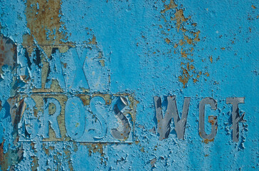 The old blue paint with letters and numbers is peeling off, dirty grunge texture. Textured beautiful abstract surface for wallpapers and backgrounds