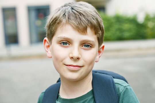 Happy preteen kid boy with backpack or satchel. Schoolkid in on the way to elementary or middle school on warm sunny summer day. Healthy child outdoors on the street in the city .
