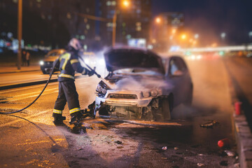 Group of fire men extinguishing and put out burning car crash after road traffic incident, fire...