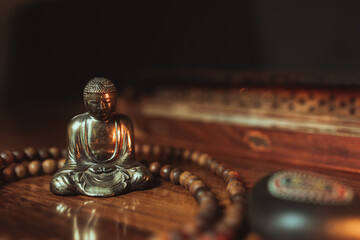 Statue of Buddha in yoga pose with wood collar and incense burner with orange warm backlight
