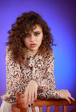 Close-up photo of young lady sittig on a chair and looking at the camera. Young beautiful curly-haired girl.