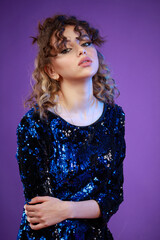 A vertical portrait of a young curly-haired girl standing on purple background