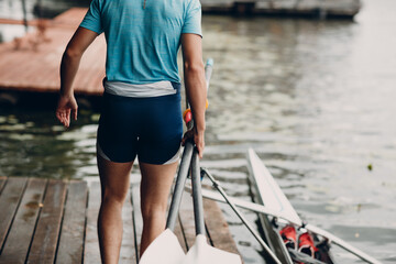 Sportsman single scull man rower prepare to competition with boat on pier