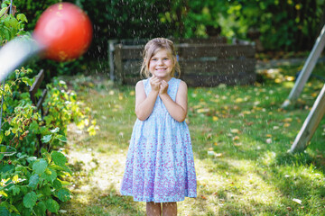 Happy little girl playing with a garden hose on hot and sunny summer evening. Preschool child...