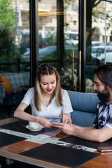 Fototapeta premium Young couple sitting at the restaurant and looking at phone