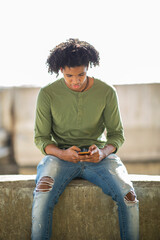 Obraz premium Man sitting outside on wall and using mobile phone