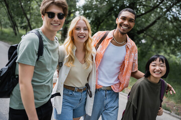happy multicultural travelers with backpacks smiling at camera outdoors.