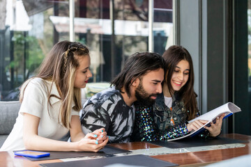 Young three friends sitting at the restaurant and reading book