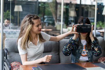 Fototapeta premium Young girl wearingVR set and her friend helping her