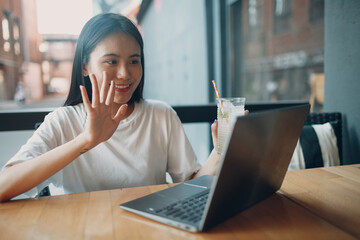 Portrait of asian woman student waving hand to camera of laptop sitting at outdoor cafe.