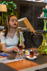 Vertical photo of young lady smoke hookah at the restaurant