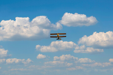 Yellow vintage plane flies in the clouds.