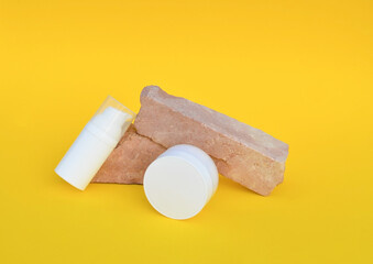 Two white plastic jars for cosmetics stands on a stone podium on an yellow background.