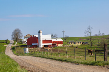 Red and white barn on an Amish farm beside a winding country road on a sunny spring day | Holmes County, Ohio