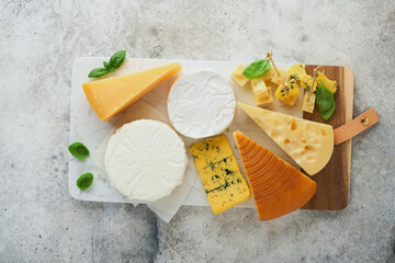 Set or assortment cheeses. Maasdam, smoked cheese, camembert, blue cheese, parmesan, brie cheese with basil and pepper on on white marble board white wooden old background. Top view. Free copy space.