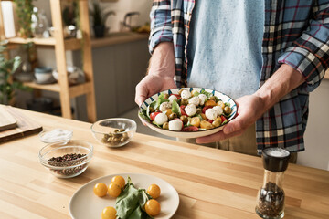 Close-up of young man holding plate with vegetable salad prepared for dinner while standing in kitchen