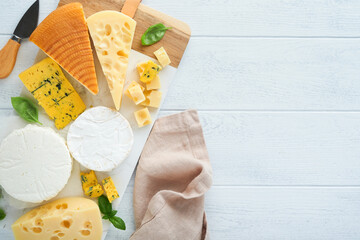 Set or assortment cheeses. Maasdam, smoked cheese, camembert, blue cheese, parmesan, brie cheese with basil and pepper on on white marble board white wooden old background. Top view. Free copy space.