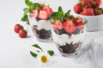 Trifles. Brownies, fresh strawberry and mascarpone cream servered in layers on glass on white background. Portion desserts. No baked brownie cheesecake with fresh berries in a glass.
