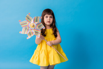 little girl in a yellow dress on a blue background holds a children's toy windmill in her hands