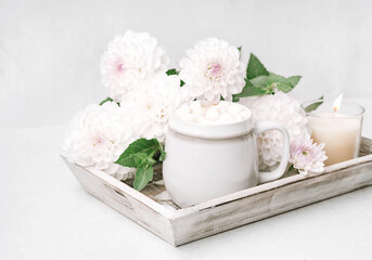 Fototapeta na wymiar Cocoa or coffee cup with marshmallow on wooden tray with white flowers. Holiday season concept. Cozy autumn home background.