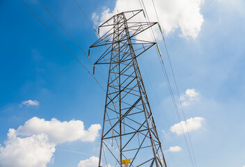 close-up of electricity power pylons and cables against a bright blue summer sky, white cloud