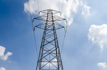 close-up of electricity power pylon and cables against a bright blue summer sky, some white cloud