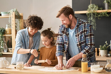 Parents teaching their little son to bake homemade pie from dough at table in kitchen