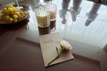 Wedding invitation with fresh white rose, grapes and two glasses with cocktail on table with reflection of guests toasting at party