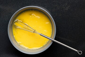 Closeup of beaten eggs in a bowl with a whisk