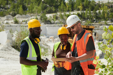 Mature man in workwear pointing at tablet screen during presentation of new working project to his colleagues or subordinates
