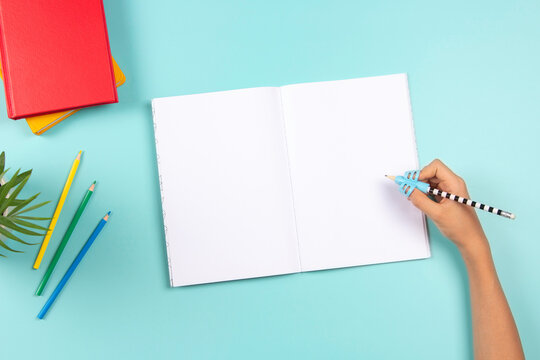 Kid Hand Using Pencil With Silicone Three Finger Pen. Top View To Hand Holding Pencil With Handwriting Correction Tool And Open Blank Notebook. School, Learning Difficulties, Writing, Education