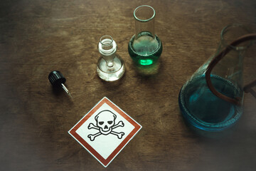Glass flasks with a dangerous toxic substance on an old table. An emblem with a skull in a red...