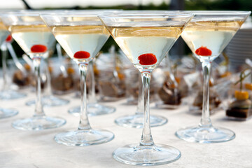 A row of glasses with champagne and cherries inside the glass are on the table.