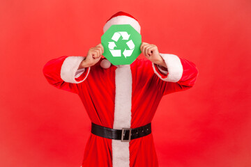Unknown man with wearing santa claus costume and red hat, standing covering his face with green...