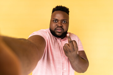 Portrait of serious aggressive man wearing pink shirt taking selfie, showing rude gesture with...