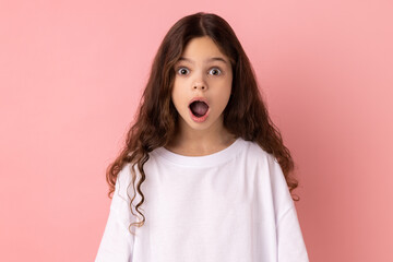 Portrait of surprised astonished little girl wearing white T-shirt looking at camera with open...