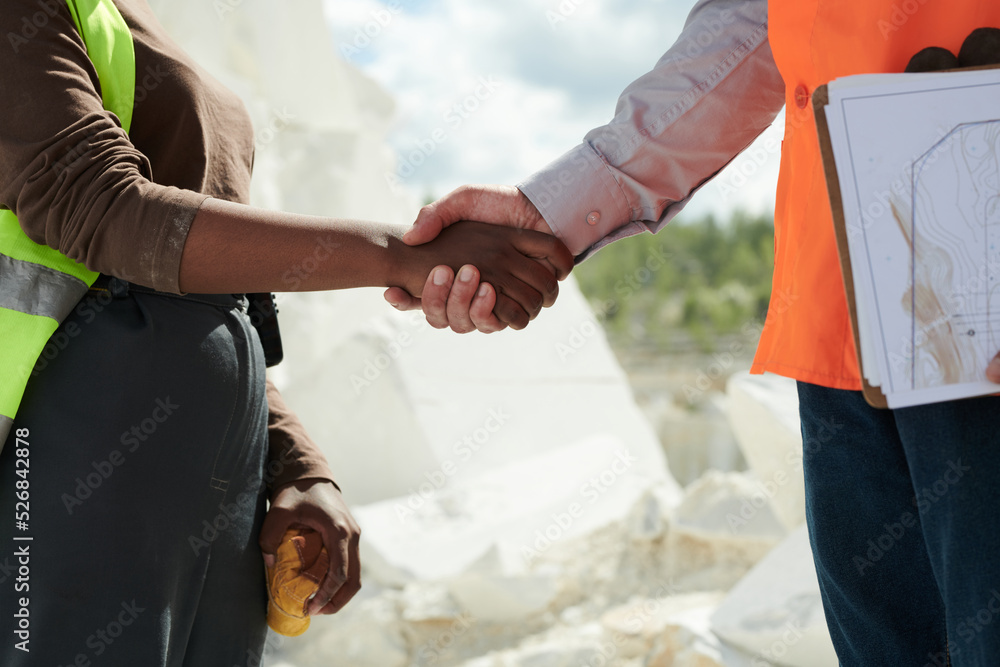 Poster close-up of two intercultural workers of marble quarry in workwear shaking hands of one another whil