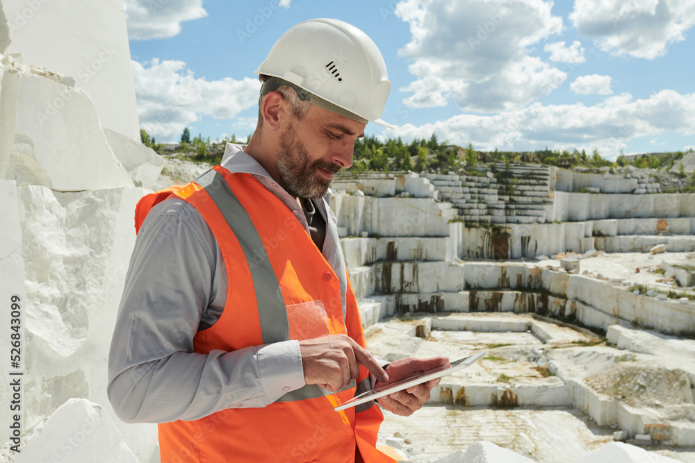 Poster side view of middle aged bearded foreman or manager with tablet pointing at screen while searching t