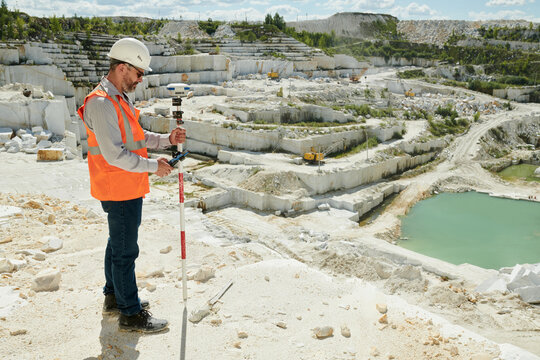 Male worker of marble quarry standing on its territory and adjusting theodolite before measuring all dimensions of the area