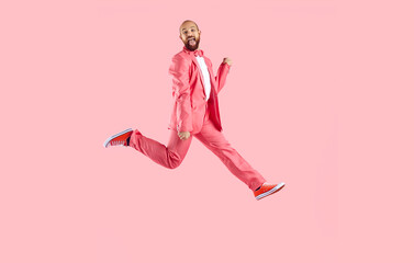 Smiling man entertainer in suit jump dance on pink studio background. Happy male performer in jacket have fun make dancing moves enjoy partying. Entertainment concept.