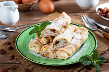Thin pancakes with cottage cheese and raisins on wooden table. Healthy traditional breakfast concept.
