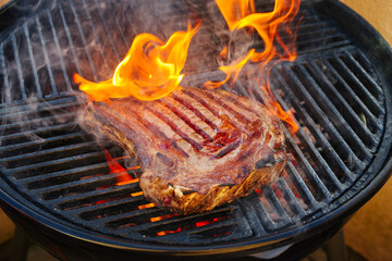Barbecue dry aged Wagyu cote de boeuf steak grilled as close-up on a charcoal grill with fire and...