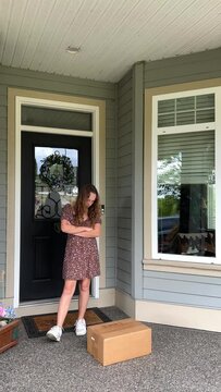 A teenage girl looks in surprise at the box that stands on her porch, she crossed her arms over her chest and is surprised at her long blond hair She doesn't remember ordering delivery