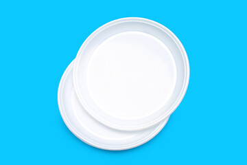 Disposable plastic plates in white on a blue background. Disposable plastic tableware for picnic or outdoor party. Plastic pollution and environmental problems