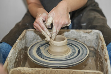 Fototapeta na wymiar Potter girl works on potter's wheel, making ceramic pot out of clay in pottery workshop. Art concept
