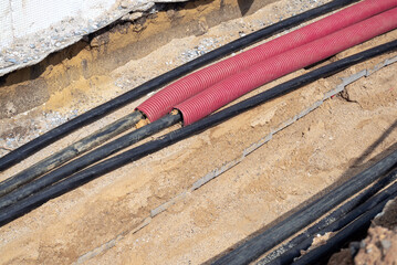 Electric cables in red corrugated pipe are buried underground on the street. infrastructure...