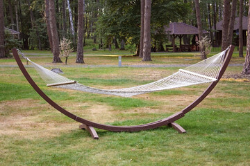 Wicker white empty hammock on a green lawn of a pine forest. Serene rest and relaxation.