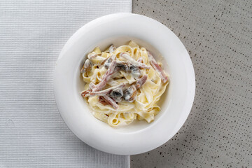 Spaghetti with ham and champignon mushrooms sprinkled with cheese. On a white plate, black background. copyspace.
